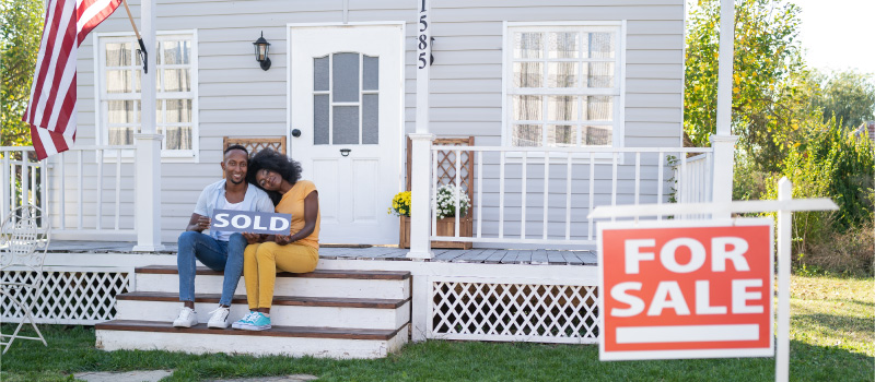 Couple sitting outside home with sold sign