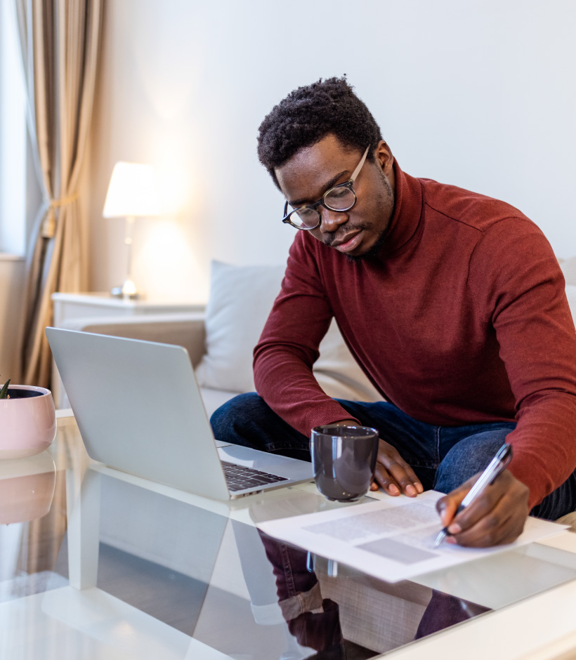person writing on paper next to laptop